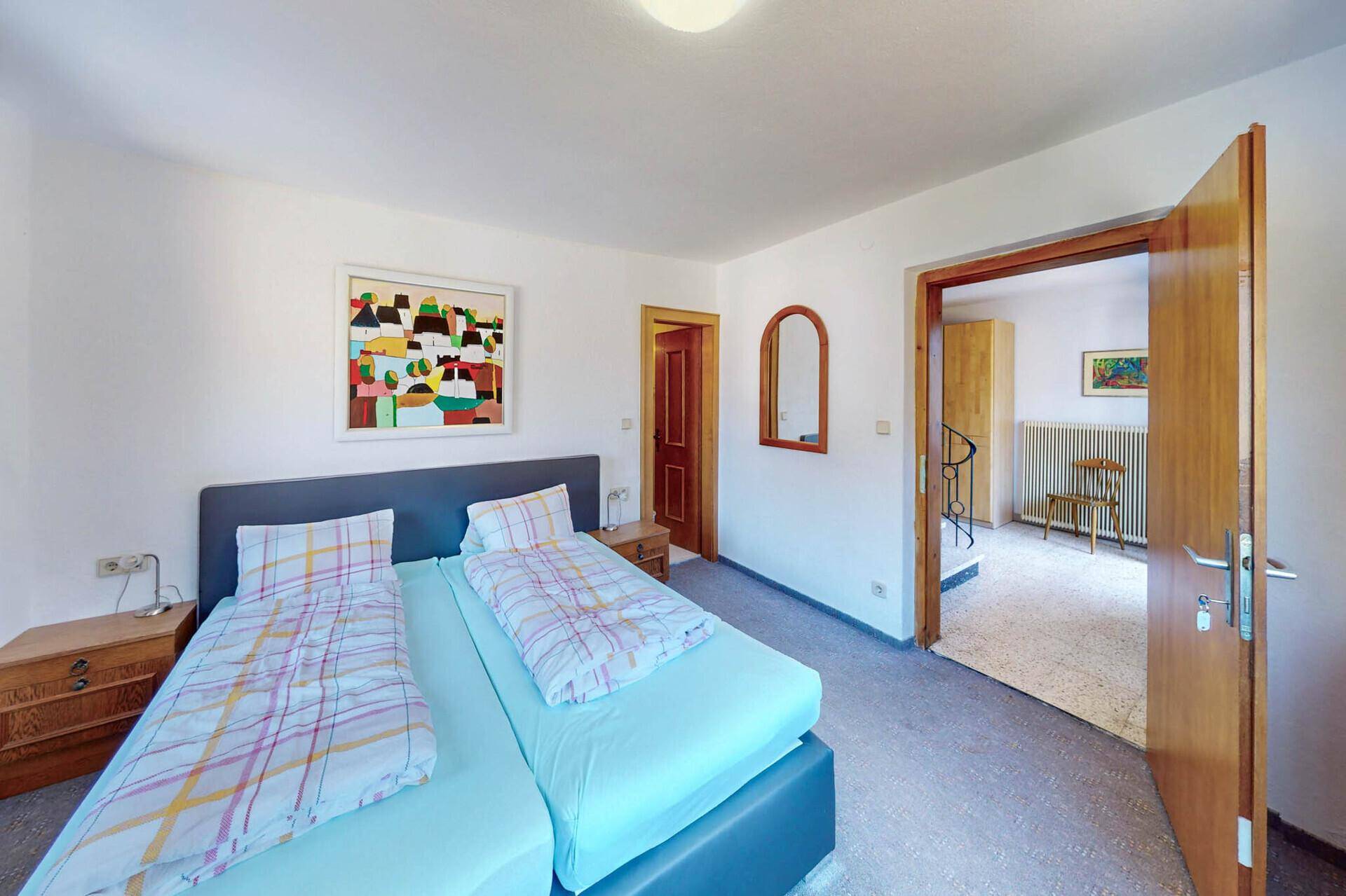 Schlafzimmer mit Doppelbett, Teppichboden und Zugang zu einem weiteren Raum.