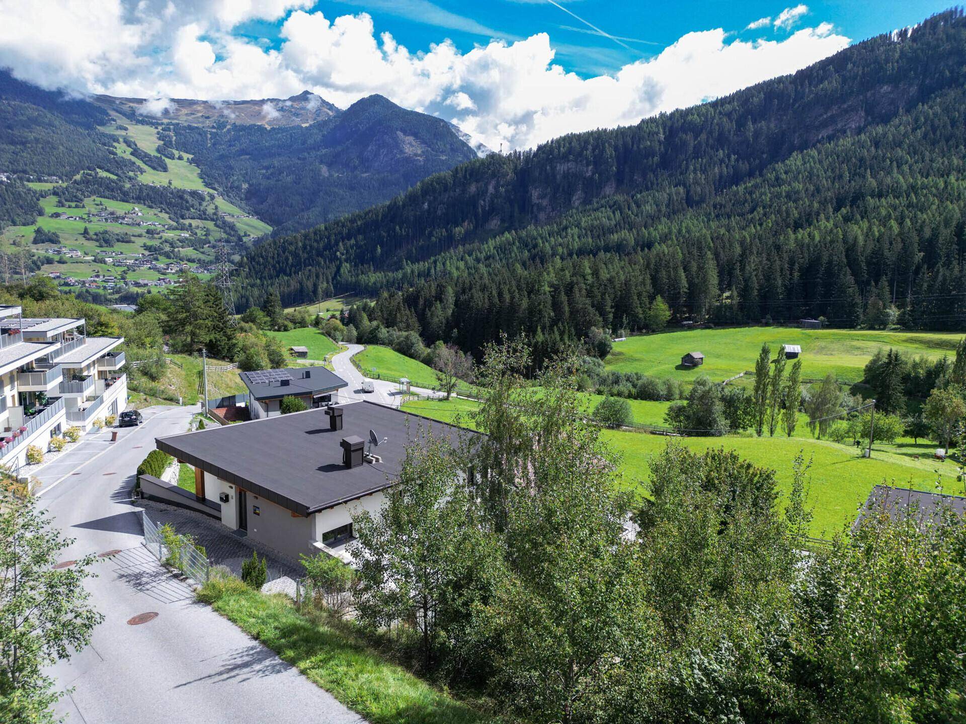 Weitläufiger Blick über ein idyllisches Tal mit Wohnhäusern, grünen Feldern und dichten Wäldern.