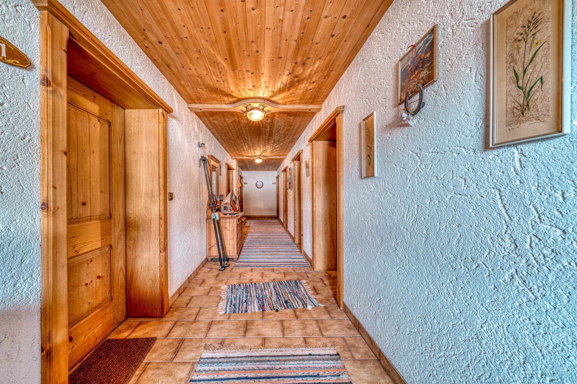 Langer Flur mit Holzdecke, Fliesenboden und traditionellen Teppichen.
