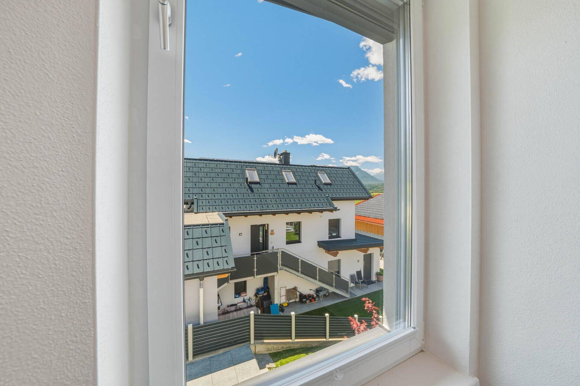 Ausblick aus dem Fenster auf ein benachbartes Haus mit Satteldach und die umliegende Landschaft.