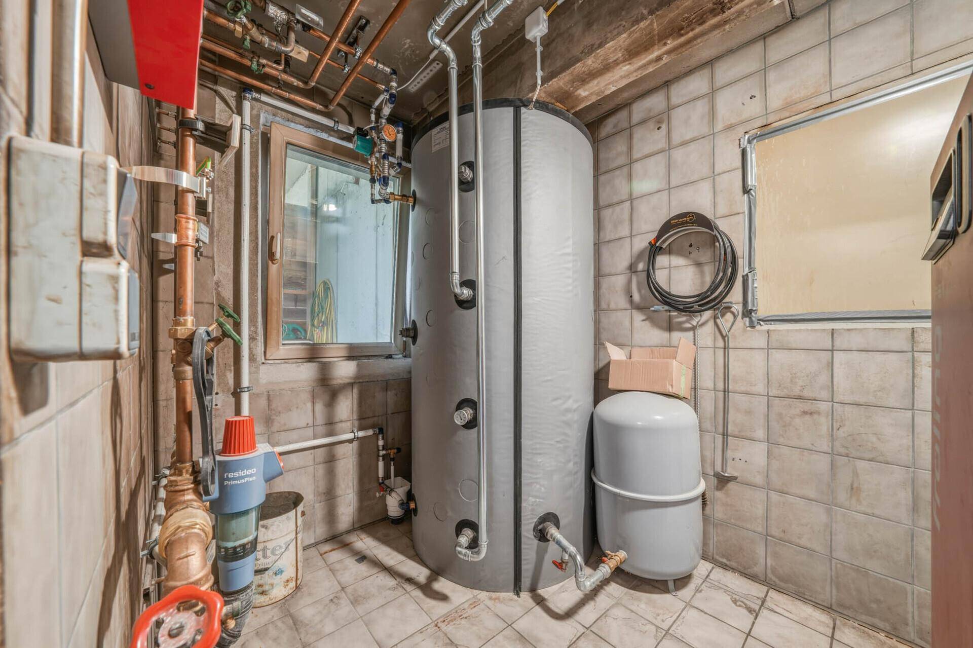 Technikraum im Keller mit großem Warmwasserspeicher und sichtbaren Rohrleitungen für die Haustechnik.