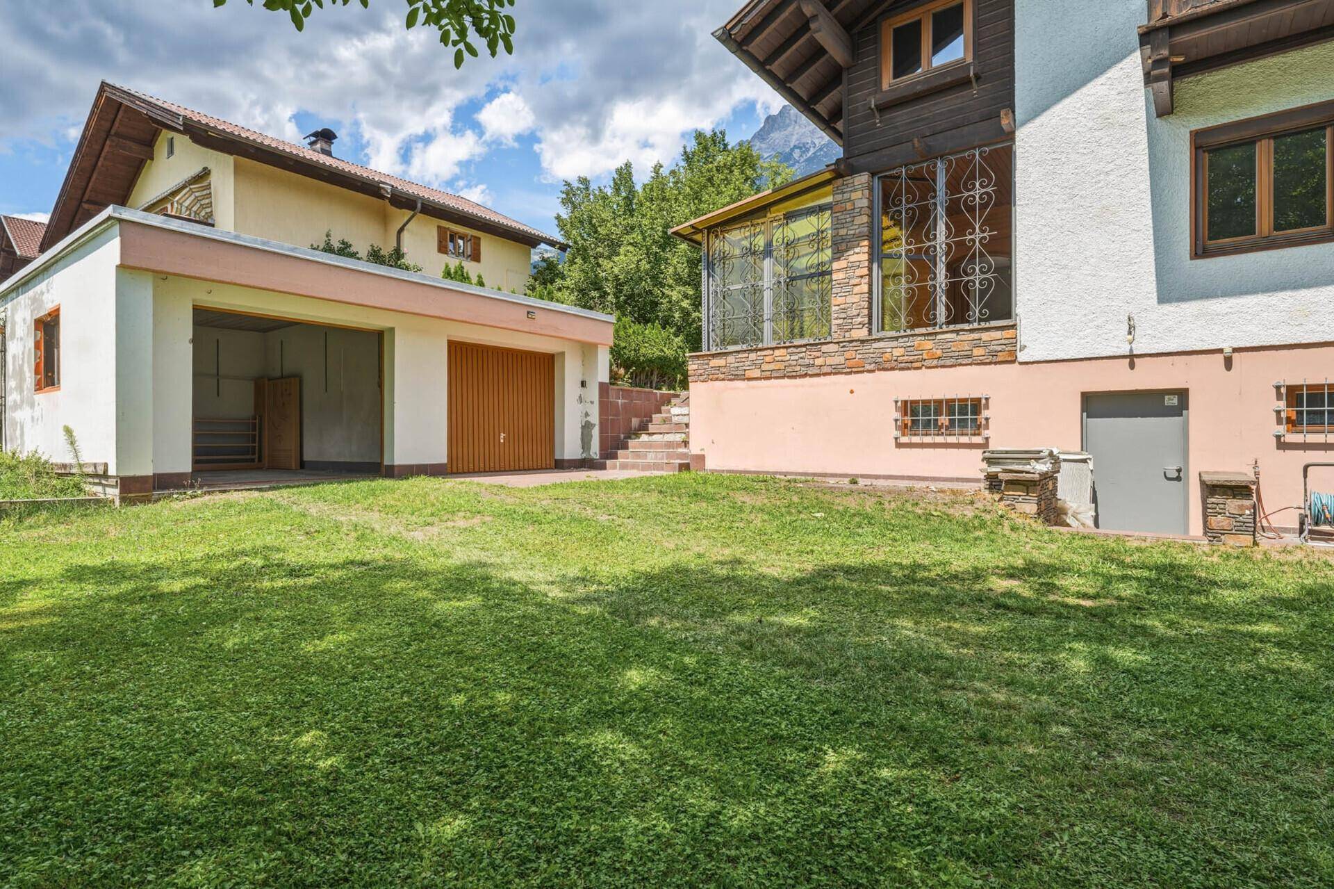 Blick vom Garten auf das Haus und die separate Garage, umgeben von Grünflächen.