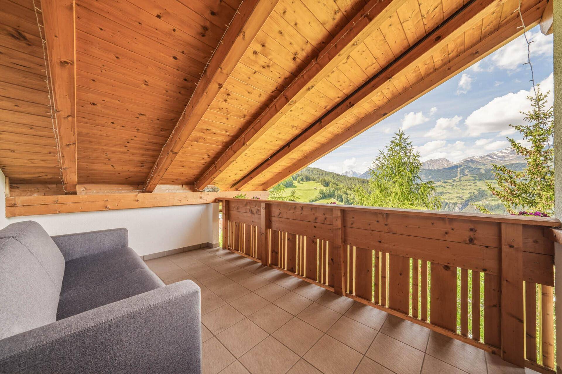 Überdachter Balkon mit Holzbalkendecke und bequemer Sitzgelegenheit, bietet einen weiten Bergblick.