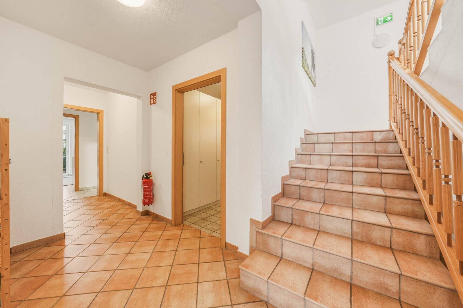 Geräumiger Flur mit Holztreppe und gefliestem Boden, der zu den Wohnbereichen führt.