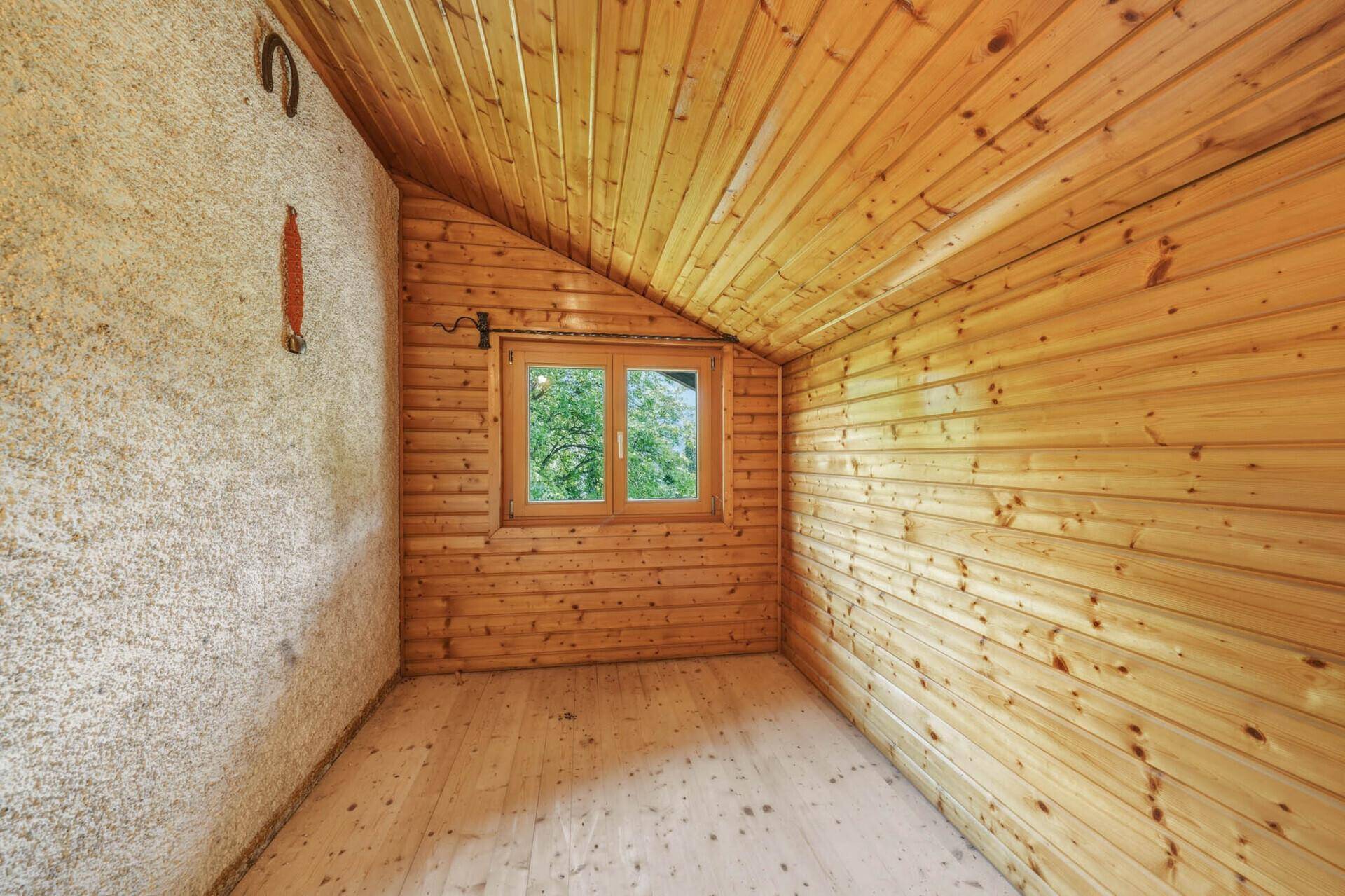 Kleiner Raum im Dachgeschoss mit Holzverkleidung, schräger Decke und einem Fenster.