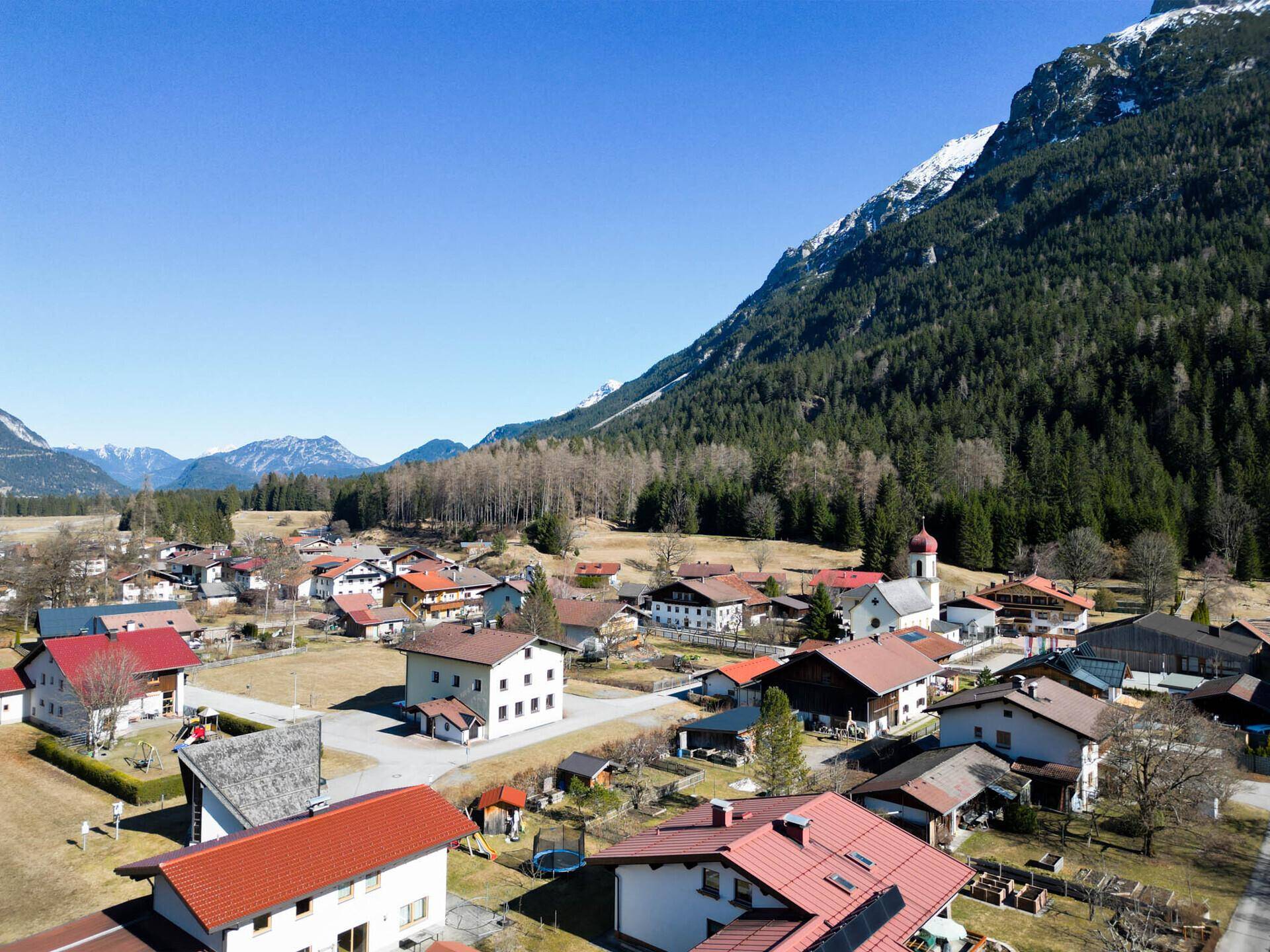 Panoramablick auf ein malerisches Dorf mit traditionellen Häusern und einer Kirche vor einer beeindruckenden Bergkulisse.