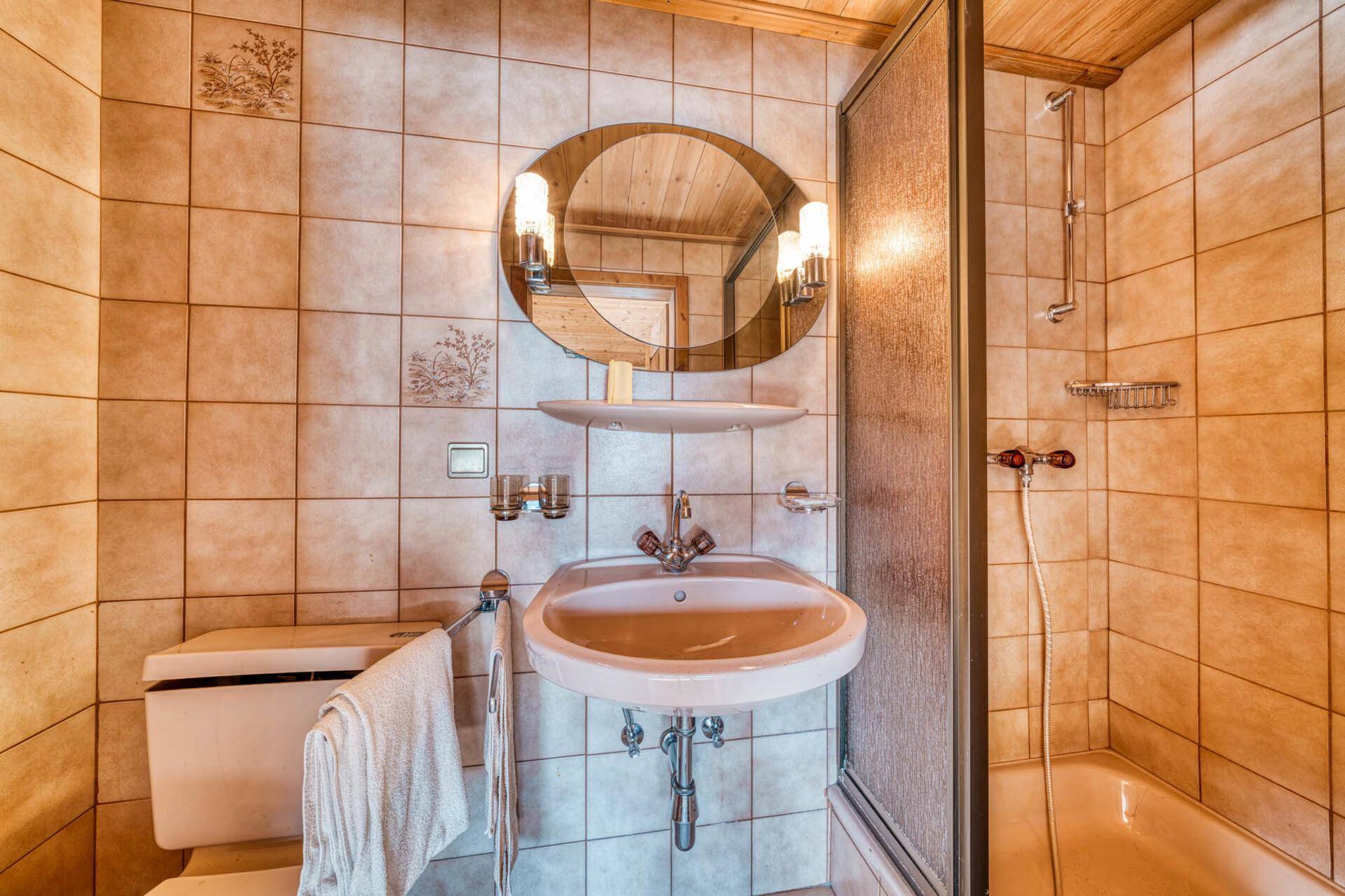 Badezimmer mit beigen Fliesen, Dusche, WC und Holzdecke.
