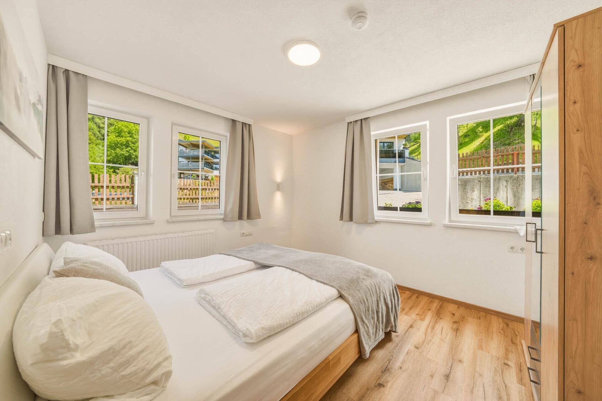 Helles Schlafzimmer mit Holzboden und mehreren Fenstern, die viel Tageslicht hereinlassen.