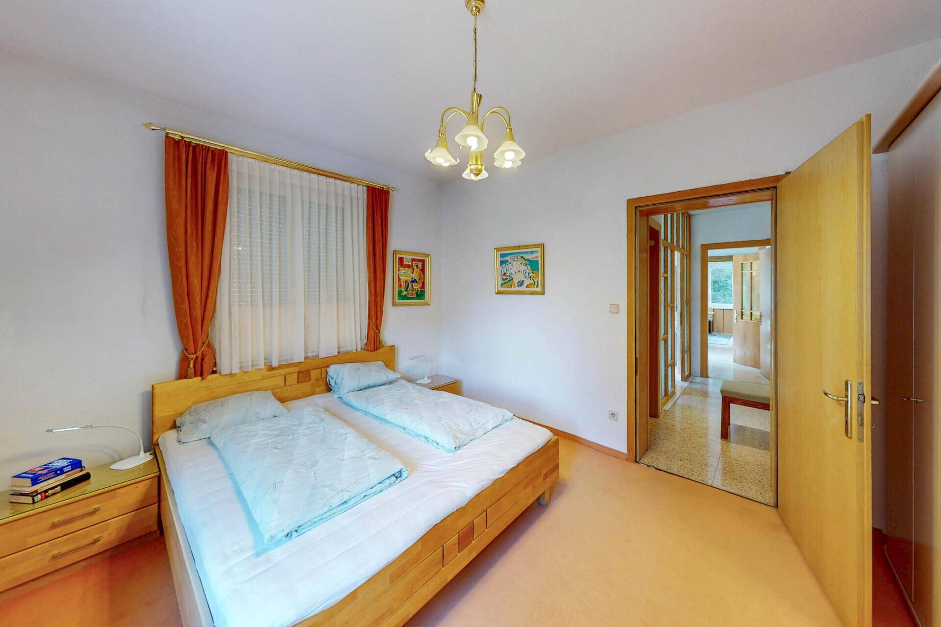 Helles Schlafzimmer mit Doppelbett, Teppichboden und Zugang zu einem Flur.