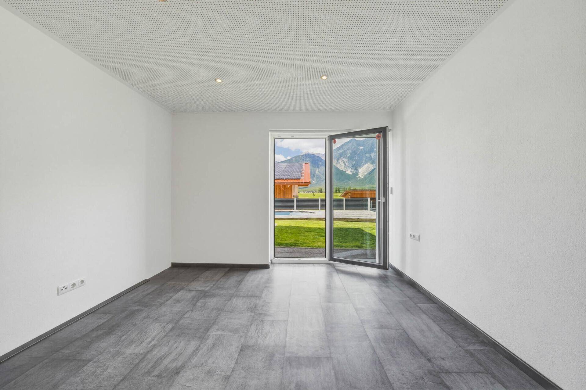Zimmer mit grauen Fliesen, weiß gestrichenen Wänden und offenem Zugang zum Garten mit Bergblick.