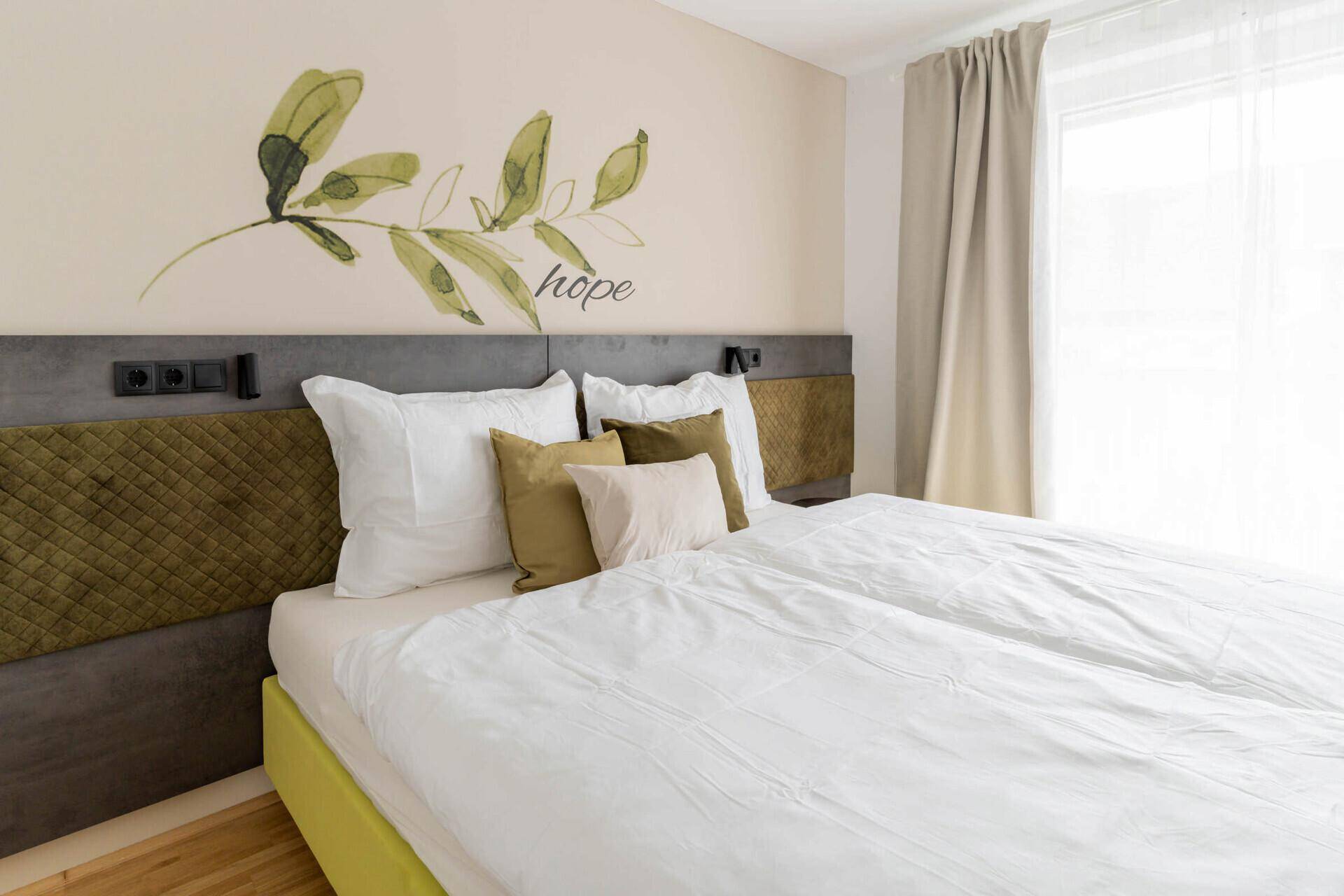 Helles Schlafzimmer mit Doppelbett, Holzboden und dekorativer Wandgestaltung.