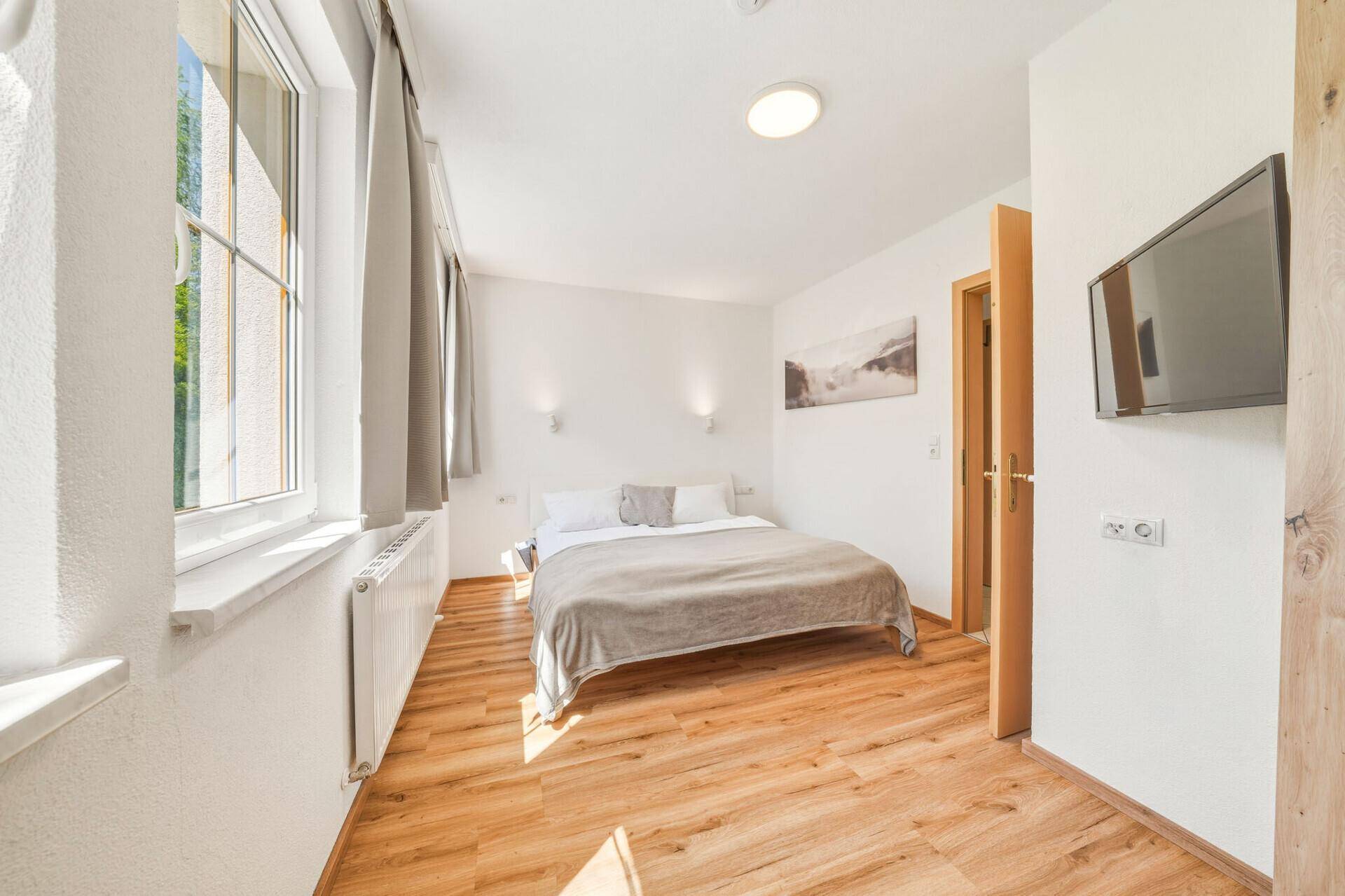 Gemütliches Schlafzimmer mit Holzboden, Doppelbett, Wandfernseher und Blick ins Grüne.