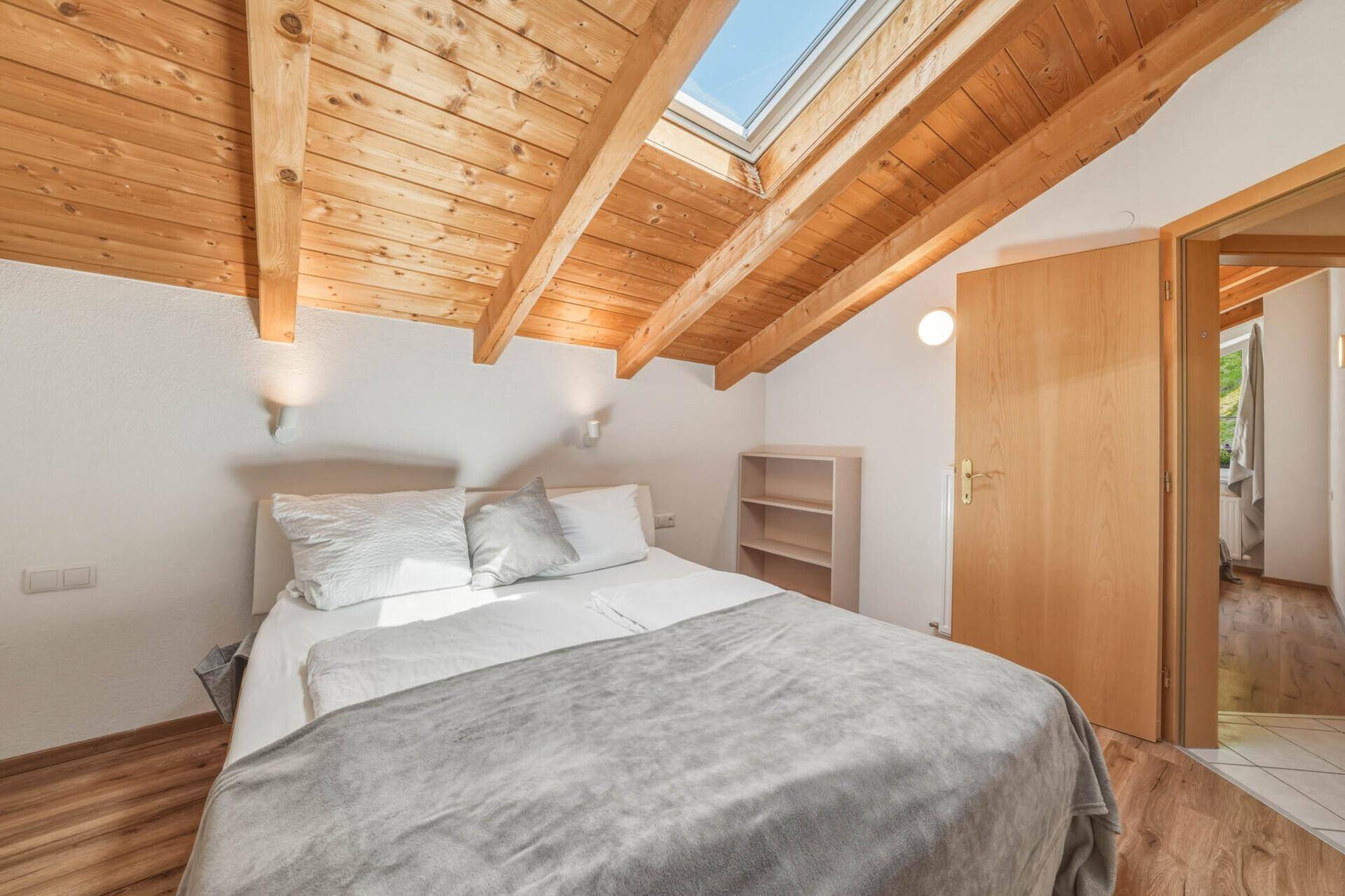 Gemütliches Schlafzimmer im Dachgeschoss mit Holzbalkendecke, Dachfenster und Holzboden.