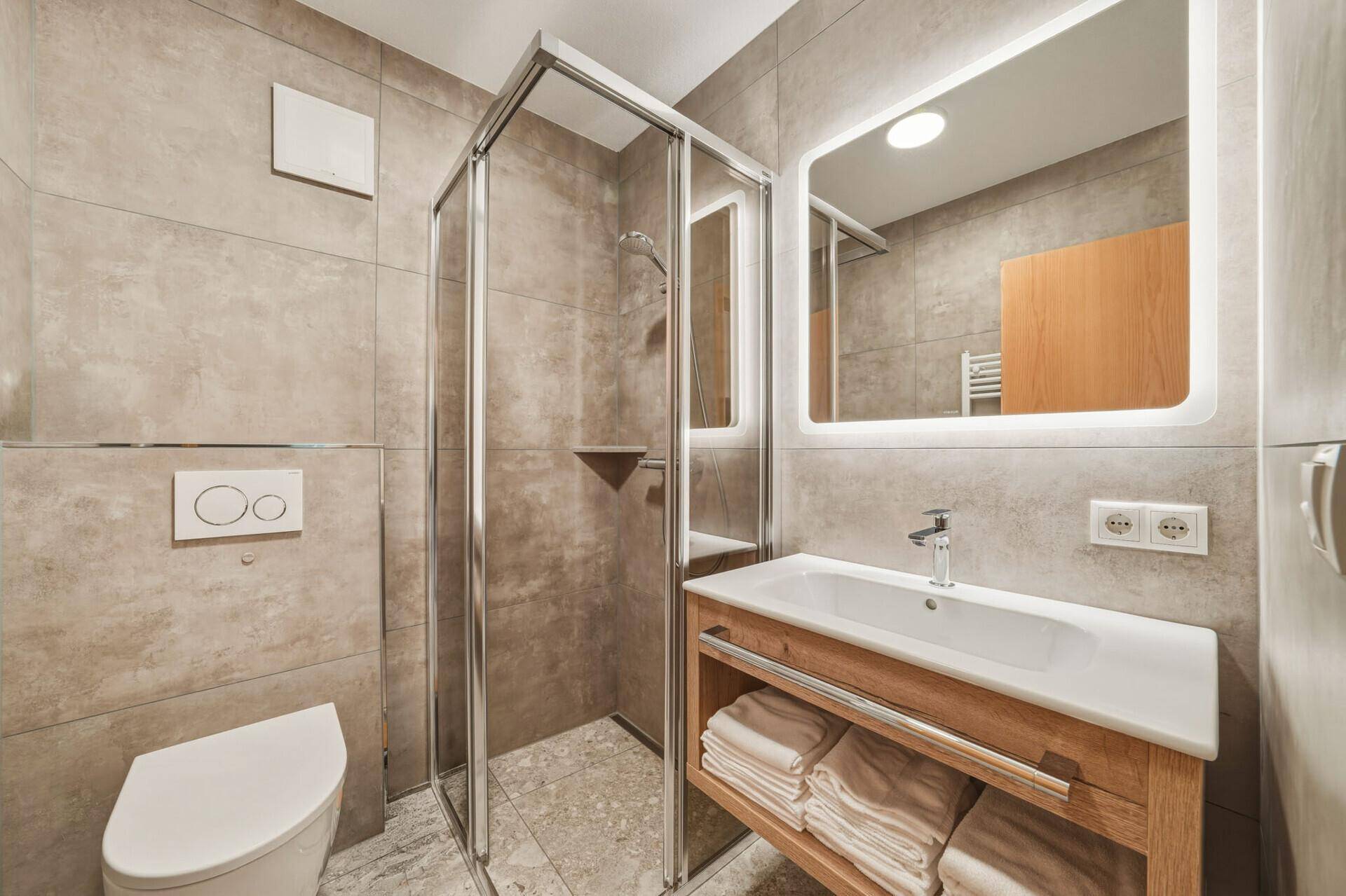 Modernes Badezimmer mit begehbarer Dusche, beleuchtetem Spiegel und eleganten Fliesen.