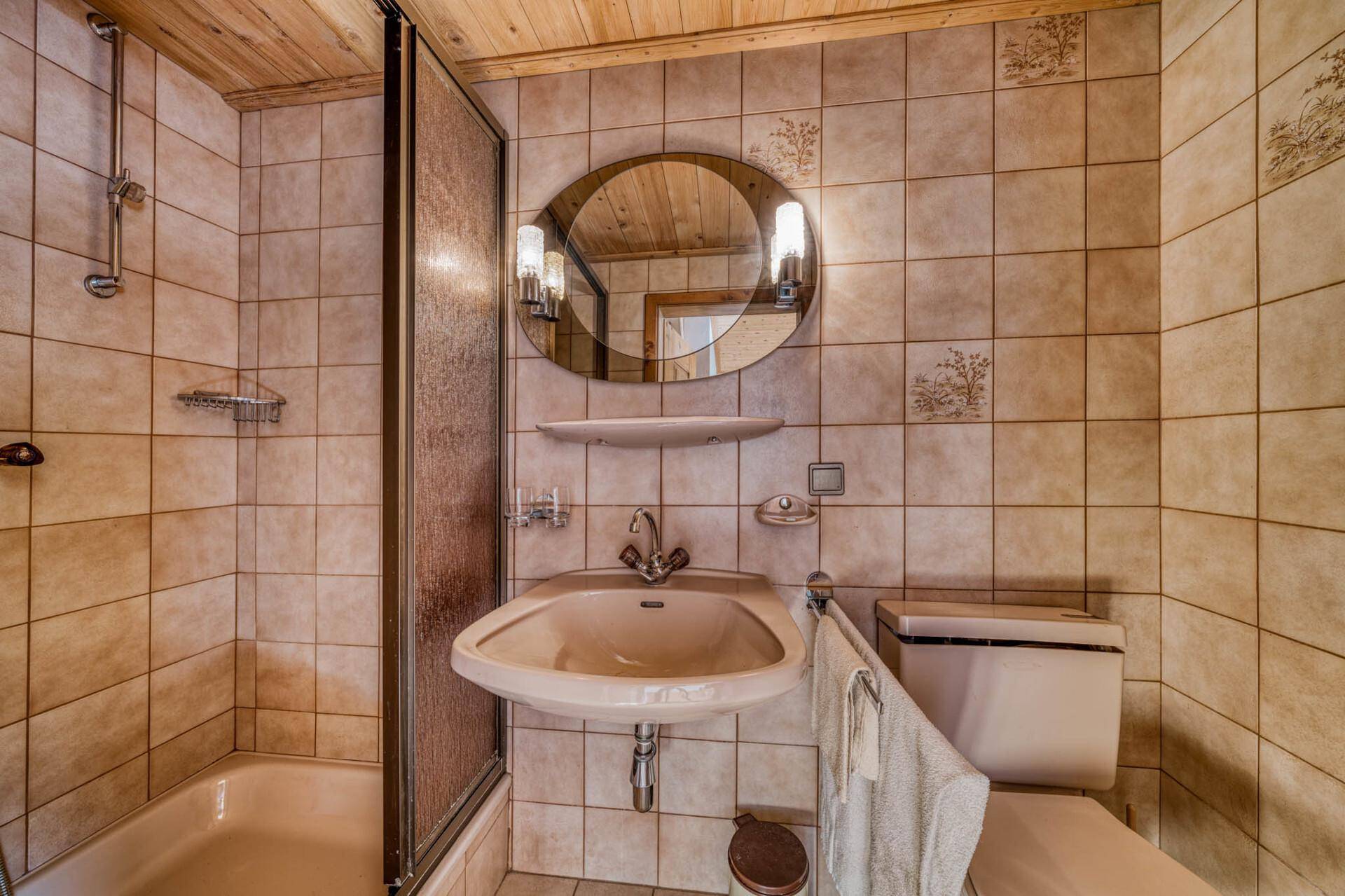 Helles Badezimmer mit beigen Fliesen, Dusche, WC und ovalem Spiegel.