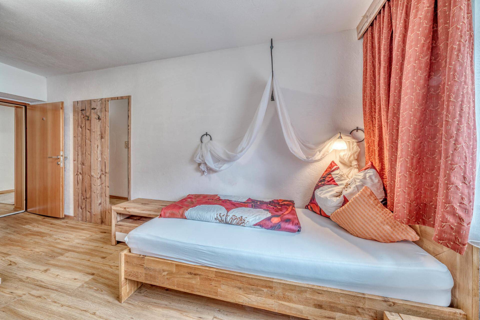 Schlafzimmer mit Einzelbett und Holzboden, helle Wände und Vorhänge, einladend.