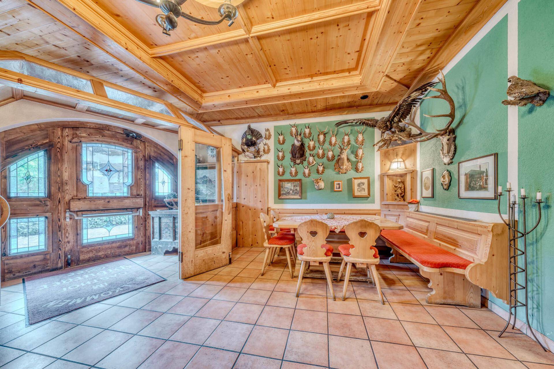 Traditioneller Essbereich mit Holzbänken, Tischen und Jagdtrophäen an der grünen Wand.