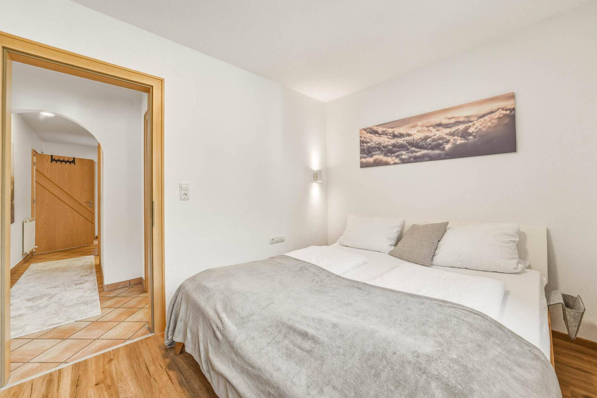 Gemütliches Schlafzimmer mit Holzboden und Zugang zu einem hellen Flur.