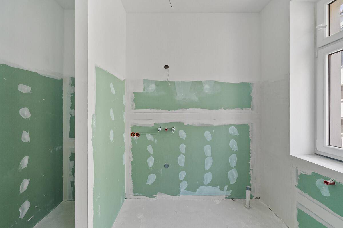 Badezimmer im Rohbau mit vorbereiteten Anschlüssen und Fenster für natürliche Belüftung.
