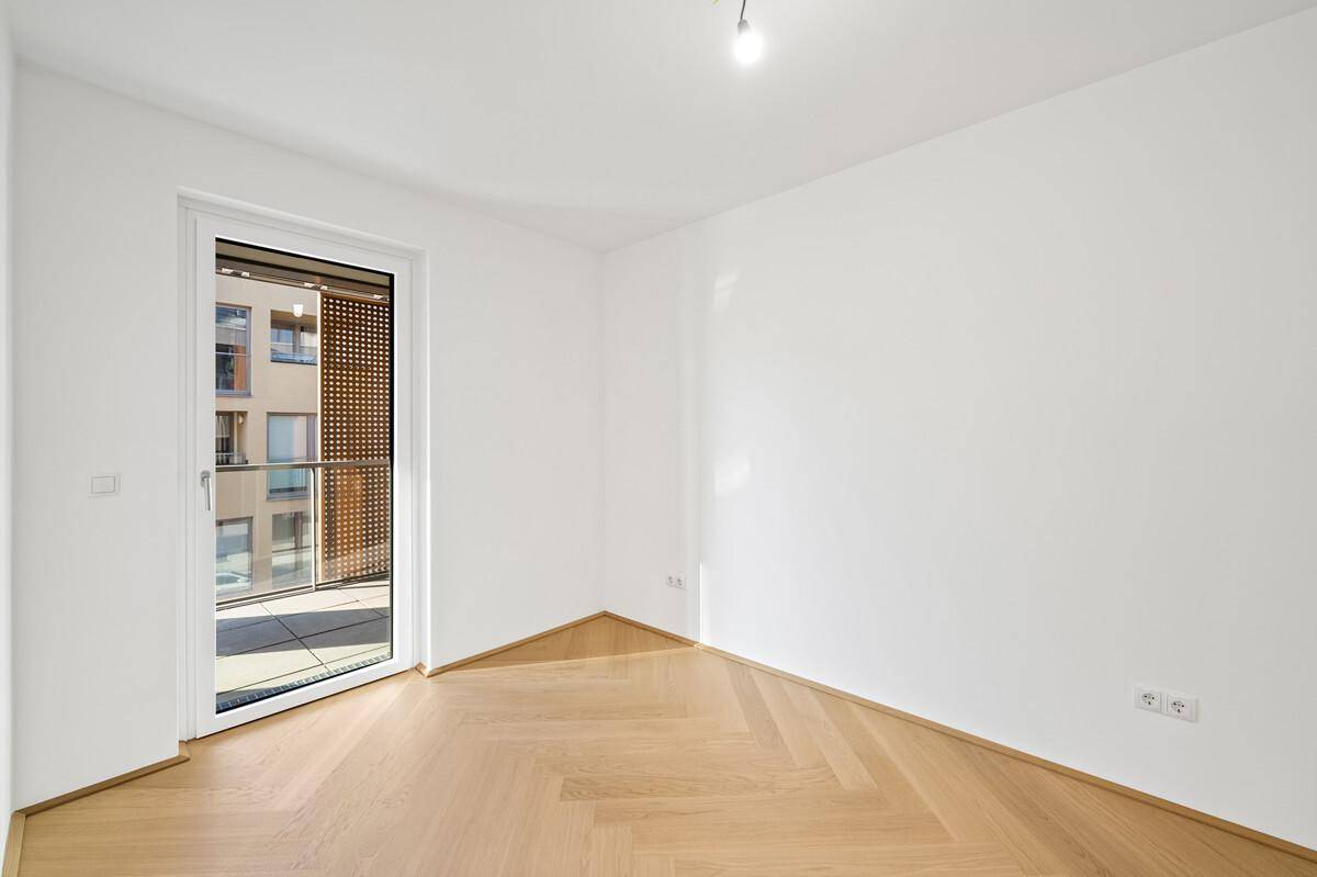 Helles Zimmer mit Fischgrätparkett und direktem Zugang zu einem Balkon mit Sichtschutz.