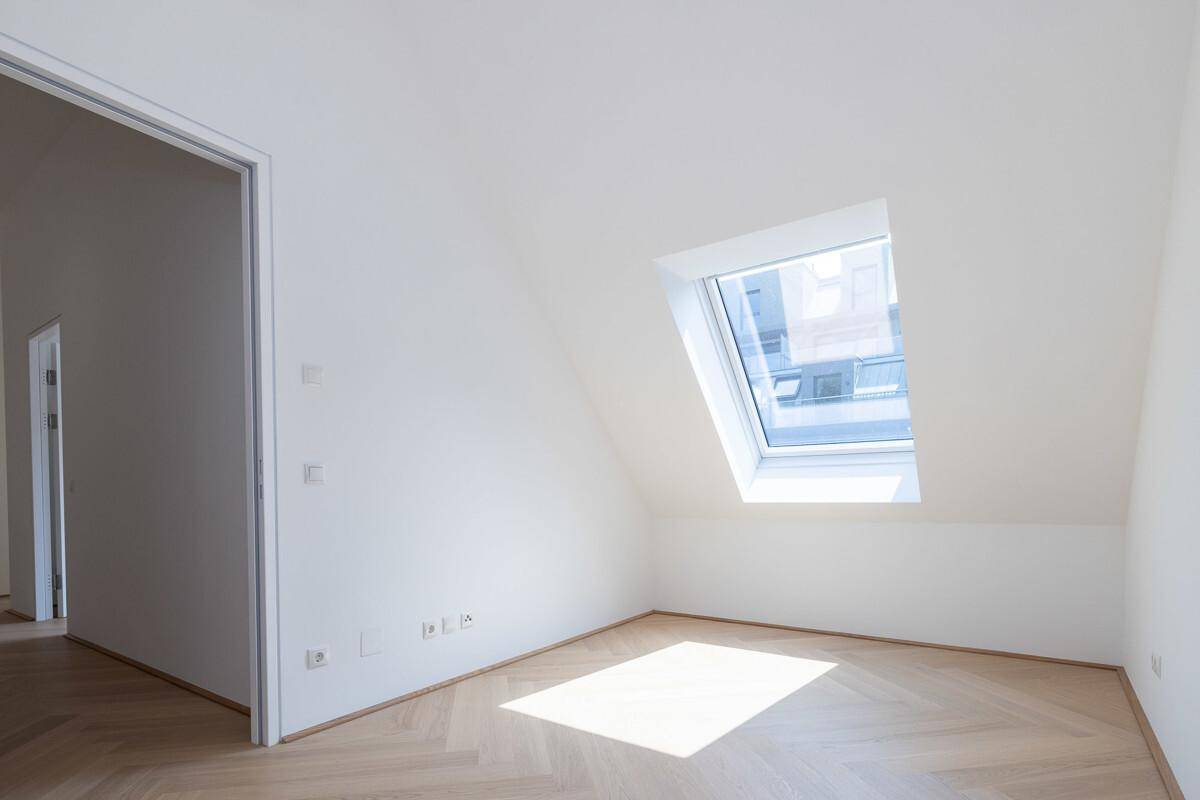 Heller Dachraum mit einem einzelnen Dachfenster und elegantem Fischgrätparkettboden.