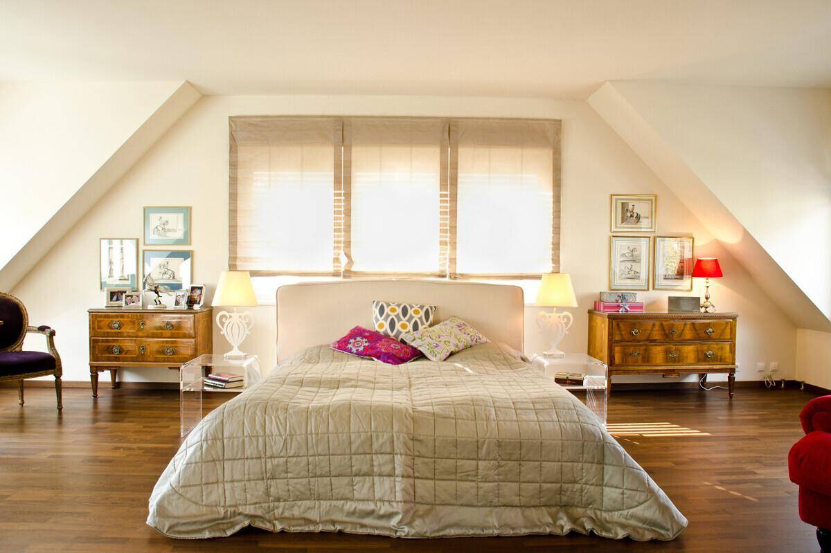Helles Schlafzimmer mit Holzboden, großem Bett und eleganten Nachttischen im Dachgeschoss.