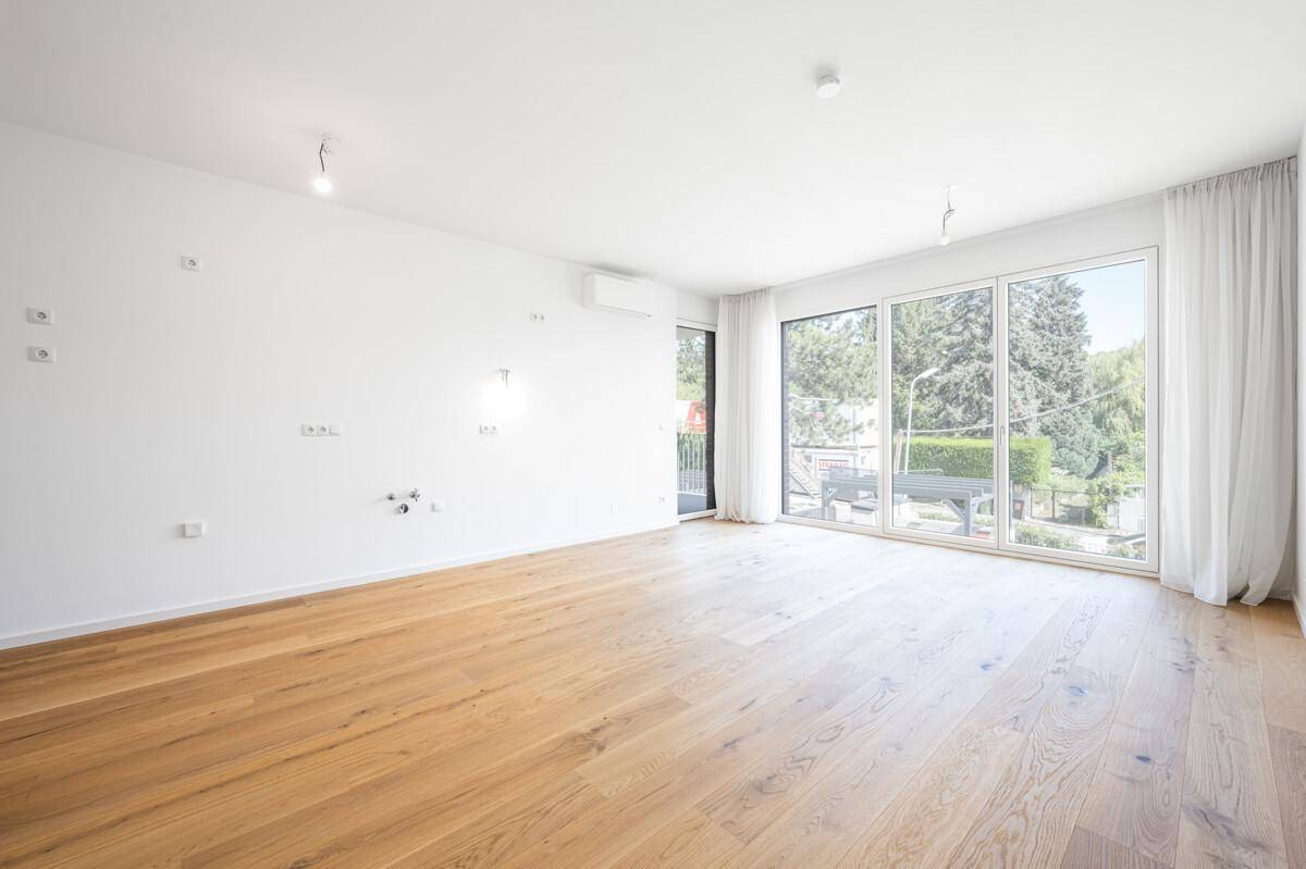 Geräumiges, helles Wohnzimmer mit Holzboden, großen Fenstern und Zugang zum Balkon.