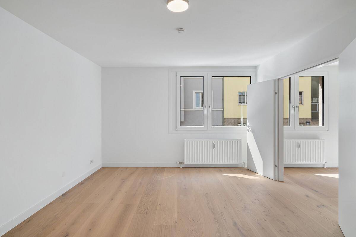 Geräumiges, helles Zimmer mit Parkettboden und Blick auf die umliegenden Gebäude.