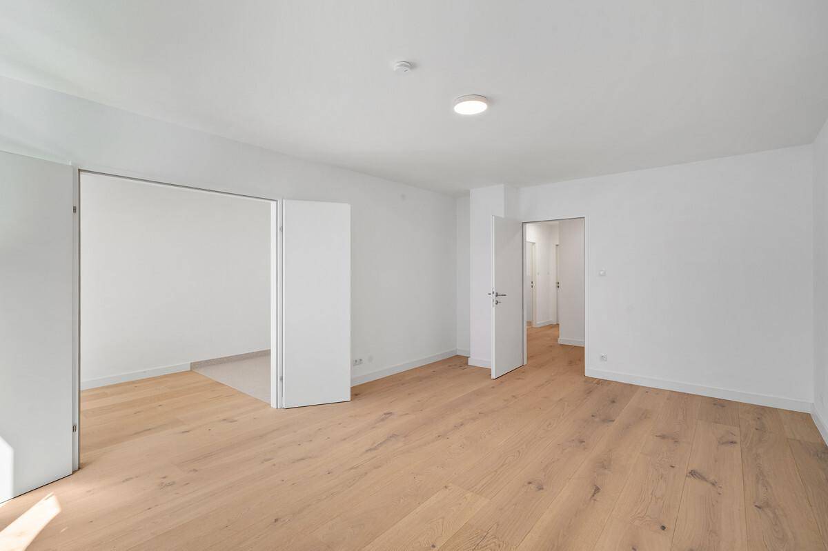 Offener Wohnbereich mit hellem Parkettboden und Zugang zu einem weiteren Zimmer.