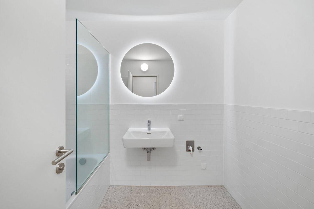 Modernes Badezimmer mit Waschtisch, beleuchtetem Spiegel und Duschbereich.