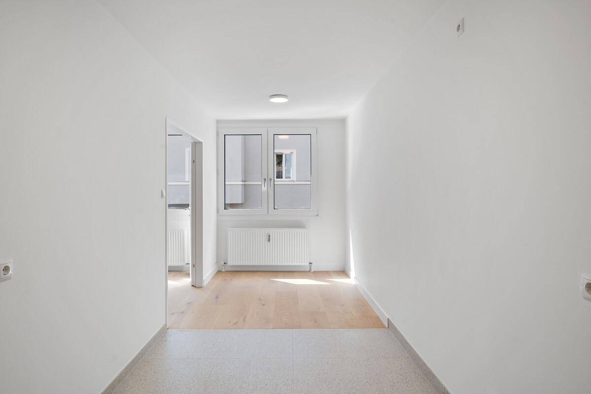 Heller Flur mit Fliesenboden, der zu einem weiteren Zimmer mit Parkett führt.