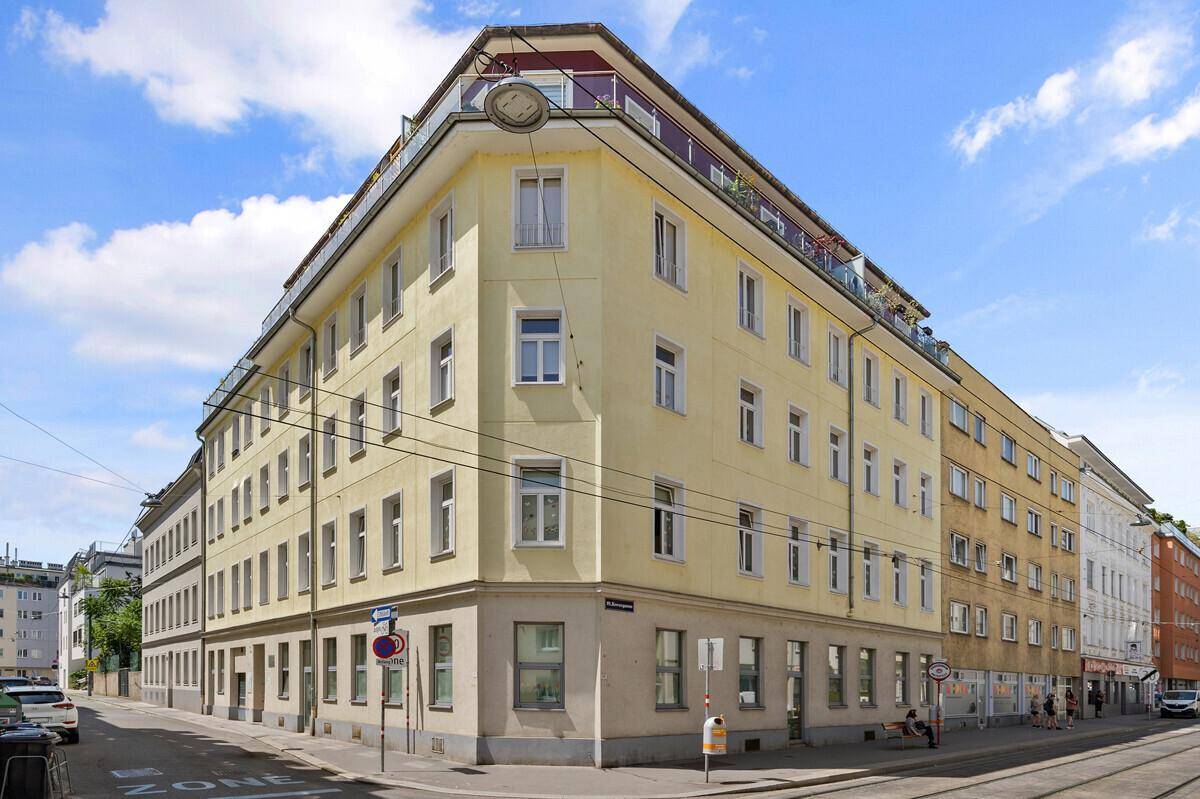 Historisches Eckgebäude mit gelber Fassade und vielen Fenstern in urbaner Umgebung.