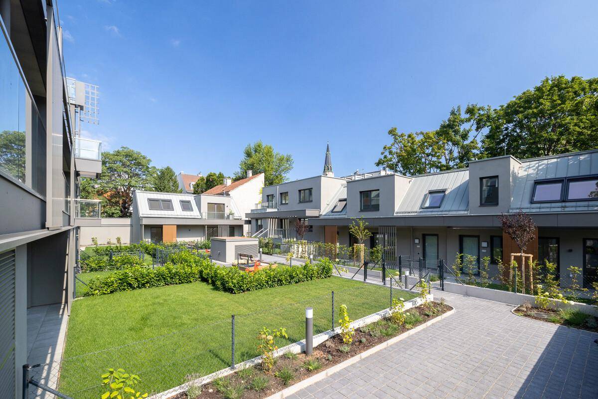 Ruhiger Innenhof mit Grünflächen, modernen Gebäuden und Blick auf einen Kirchturm.