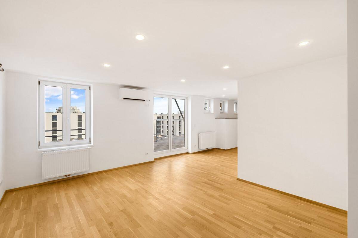 Geräumiger Wohnbereich mit Holzboden, viel Tageslicht und Blick auf die Umgebung.