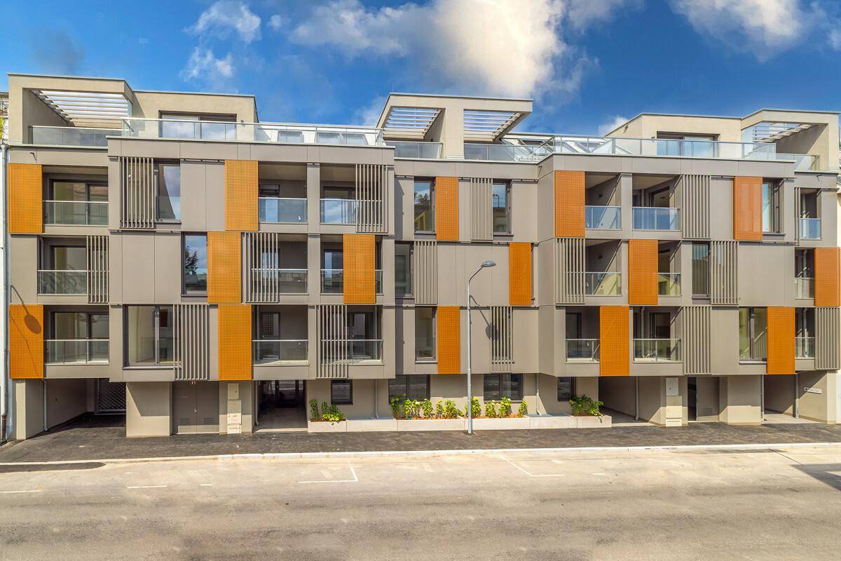 Moderne Wohnanlage mit mehreren Etagen, Balkonen und stilvoller Fassadengestaltung in Grau und Orange.