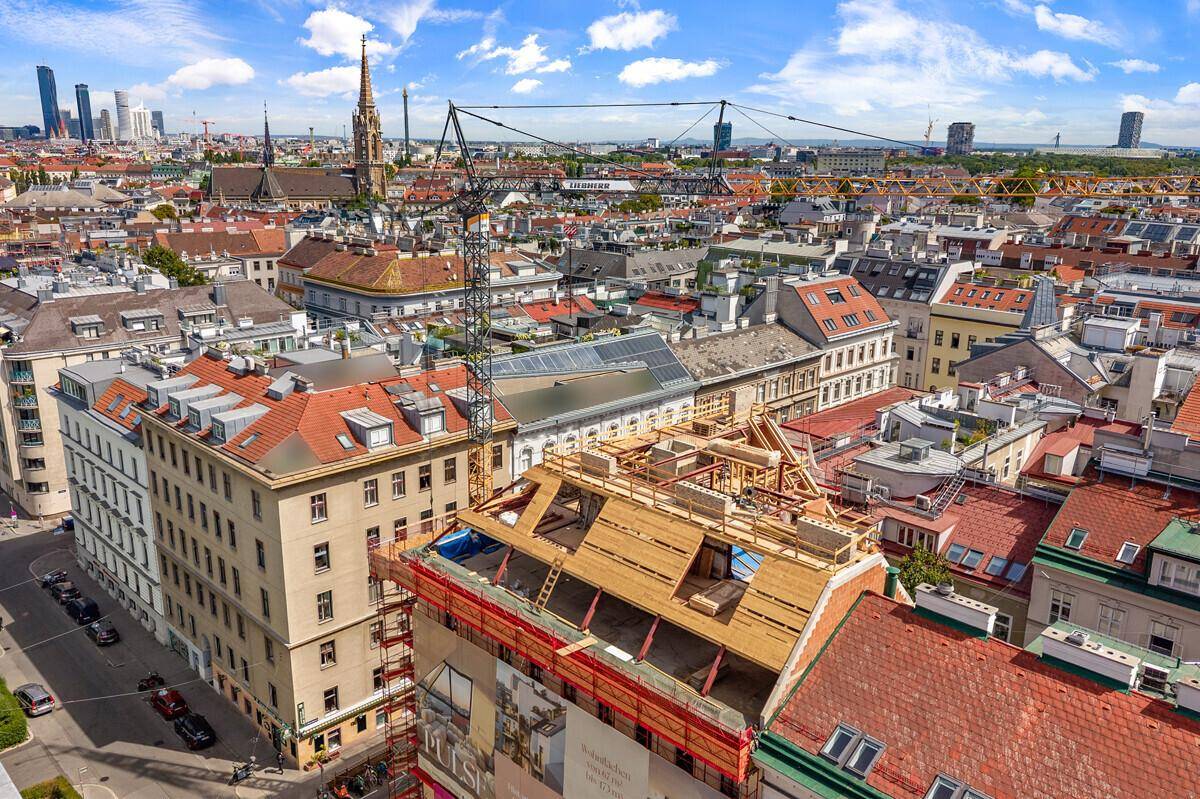 Weitläufige Luftaufnahme der Baustelle mit Dachausbau und Blick über die Dächer der Stadt.