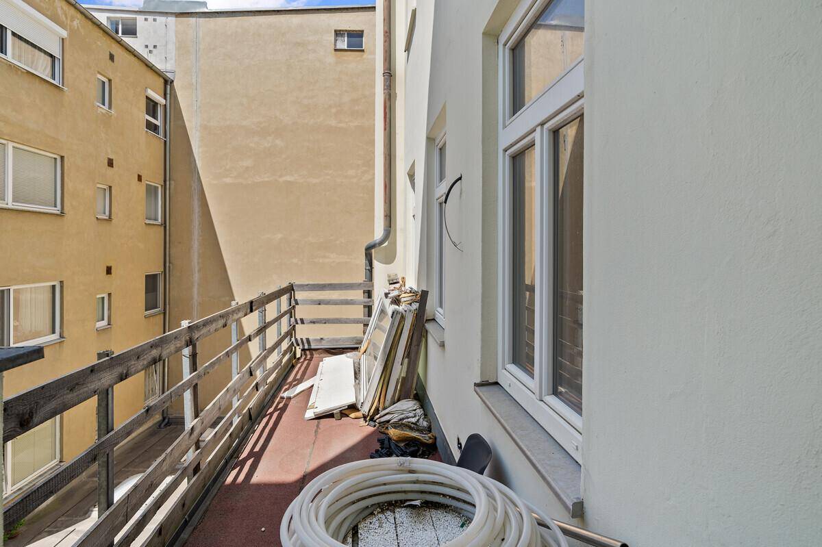 Balkon im Rohzustand mit Holzgeländer und Blick auf den Innenhof, bereit zur Fertigstellung.