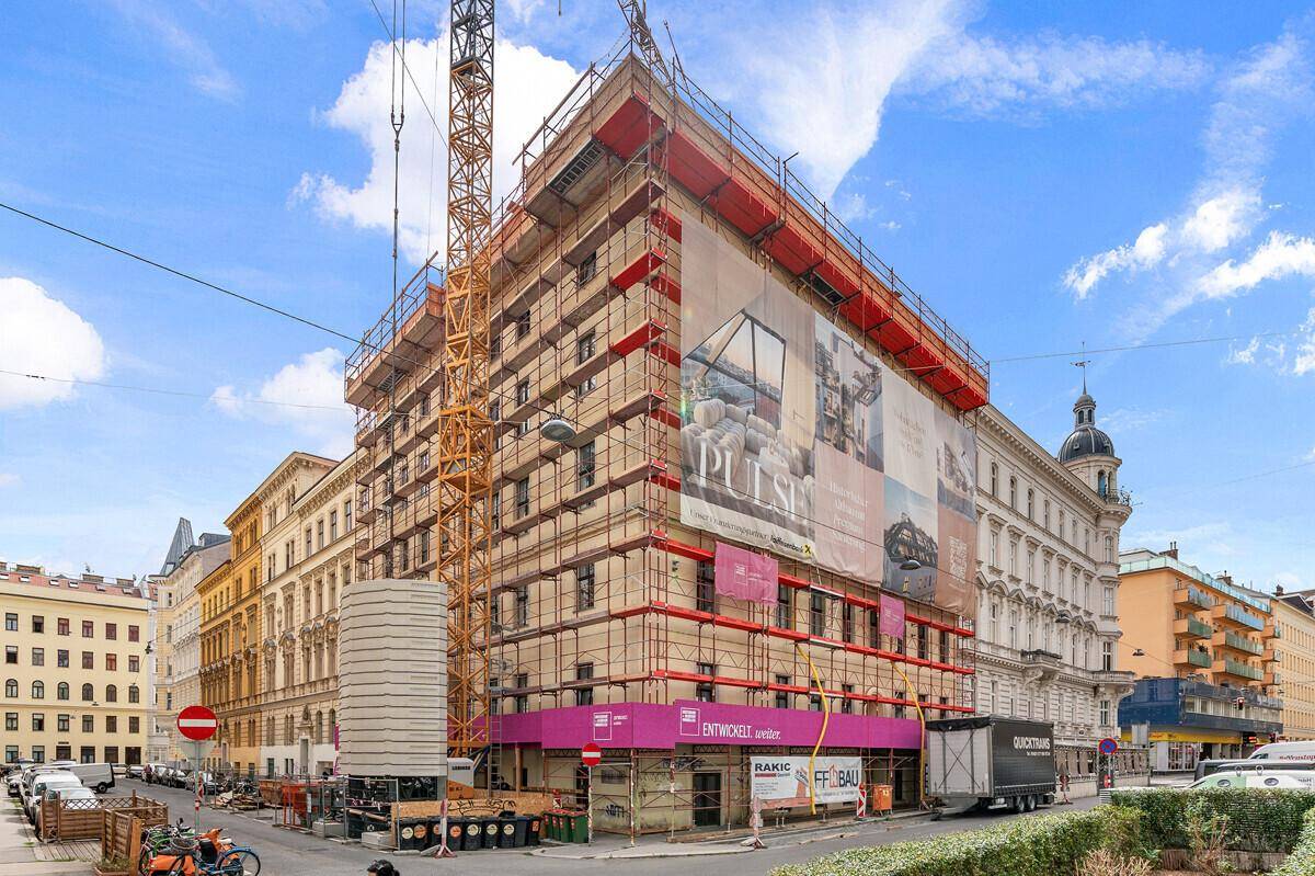 Gebäude im Bau mit Gerüst und Werbebanner an einer städtischen Straße.
