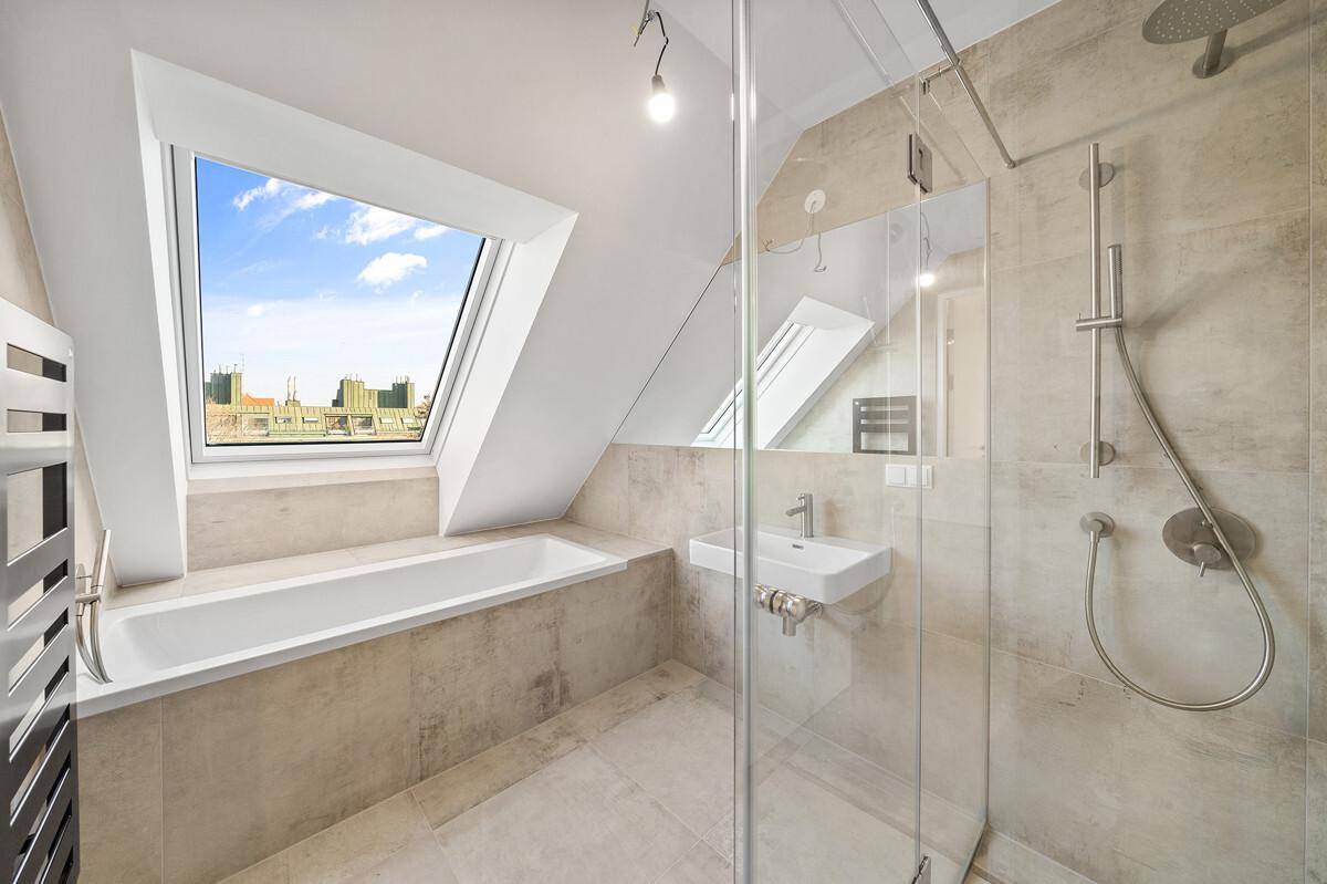 Modernes Badezimmer mit Badewanne, Dusche, Dachfenster und hellen Fliesen in Beige.