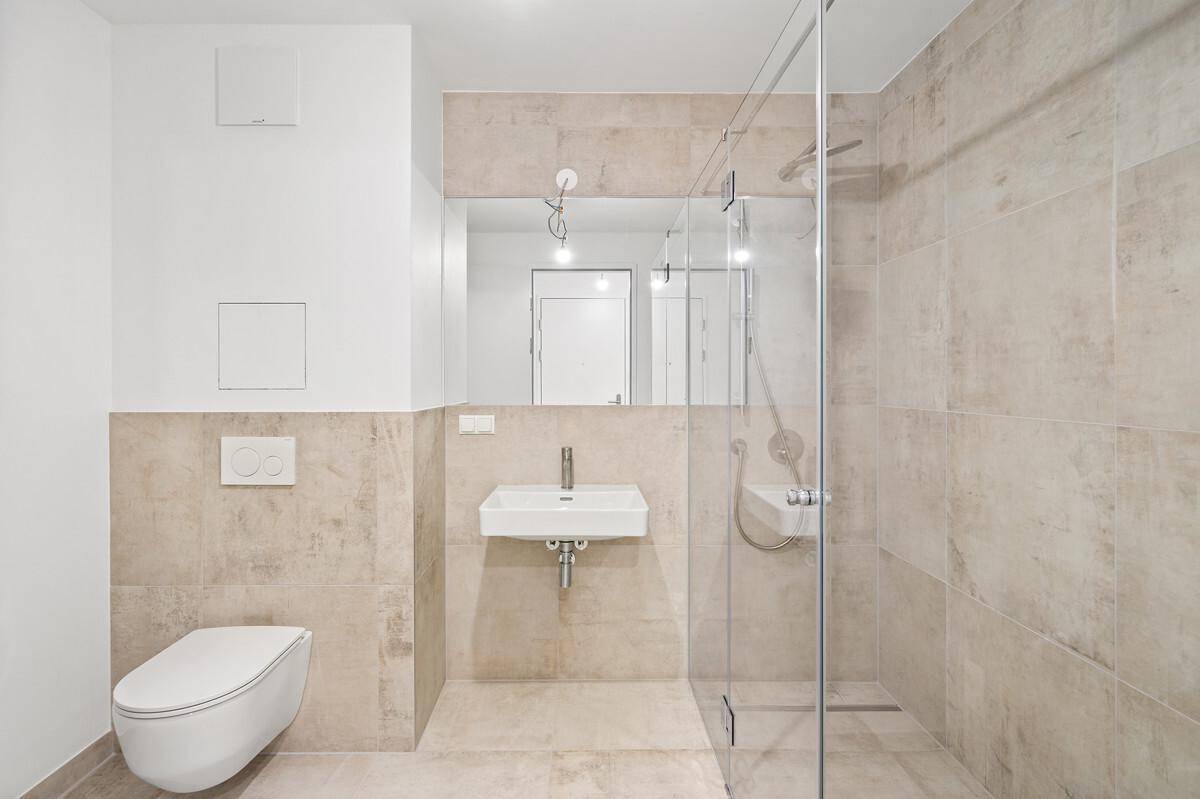 Modernes Badezimmer mit beigefarbenen Fliesen, wandhängendem WC und einer begehbaren Dusche.
