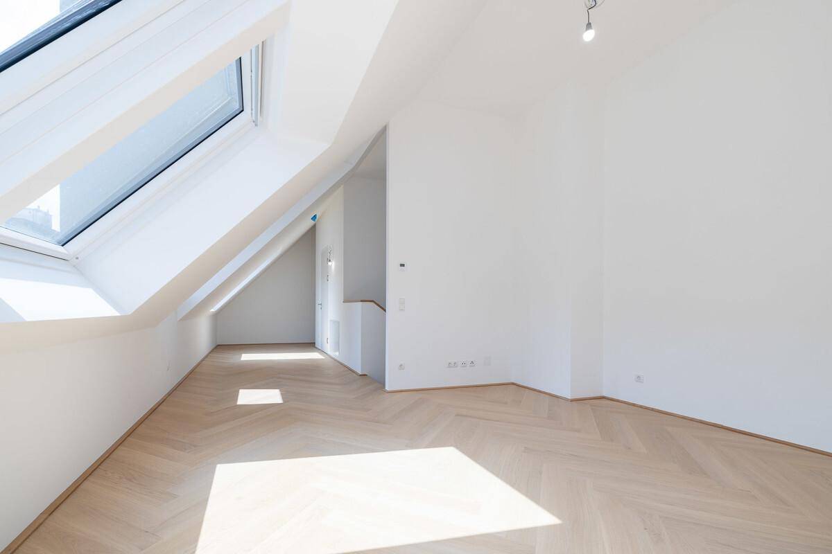 Geräumiger Dachraum mit großen Dachfenstern, die viel Tageslicht hereinlassen, und Parkettboden.