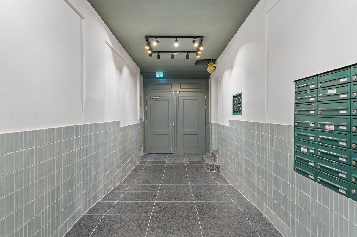 Heller Flur mit doppelter Eingangstür, grauen Bodenfliesen und grünen Briefkastenanlagen.