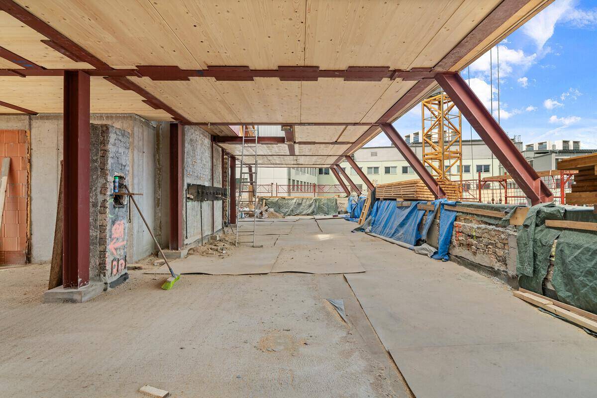 Dachgeschoss im Rohbau mit Stahlträgern, Ziegelwänden und viel Tageslicht.
