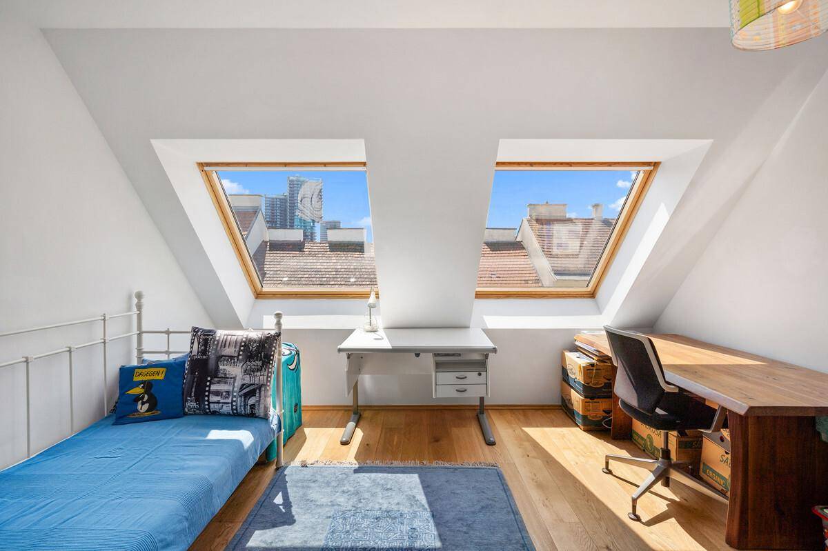 Helles Schlafzimmer im Dachgeschoss mit zwei Dachfenstern und Holzboden.