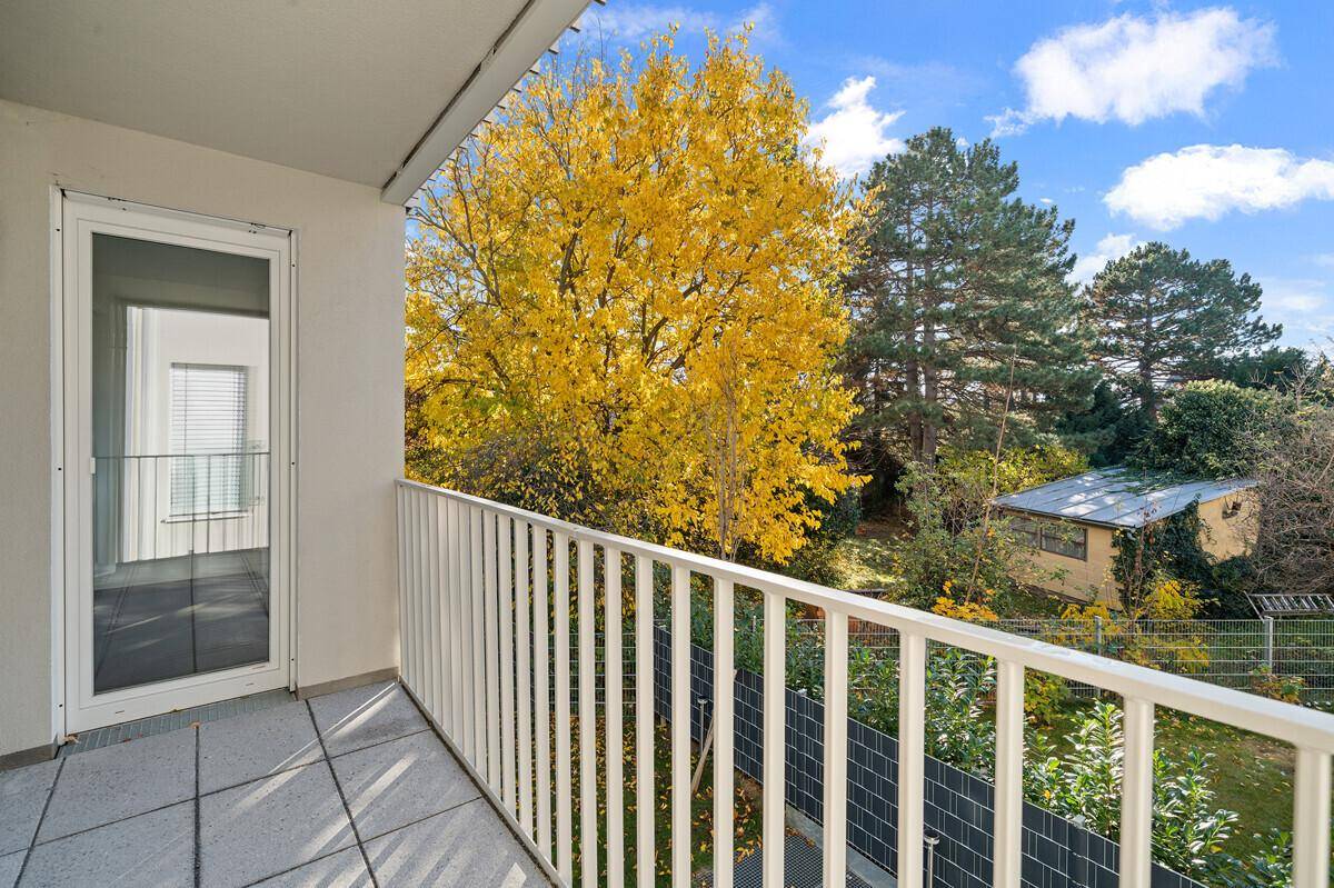 Geräumiger Balkon mit Fliesenboden, weißem Geländer und Blick ins Grüne mit Herbstbäumen.