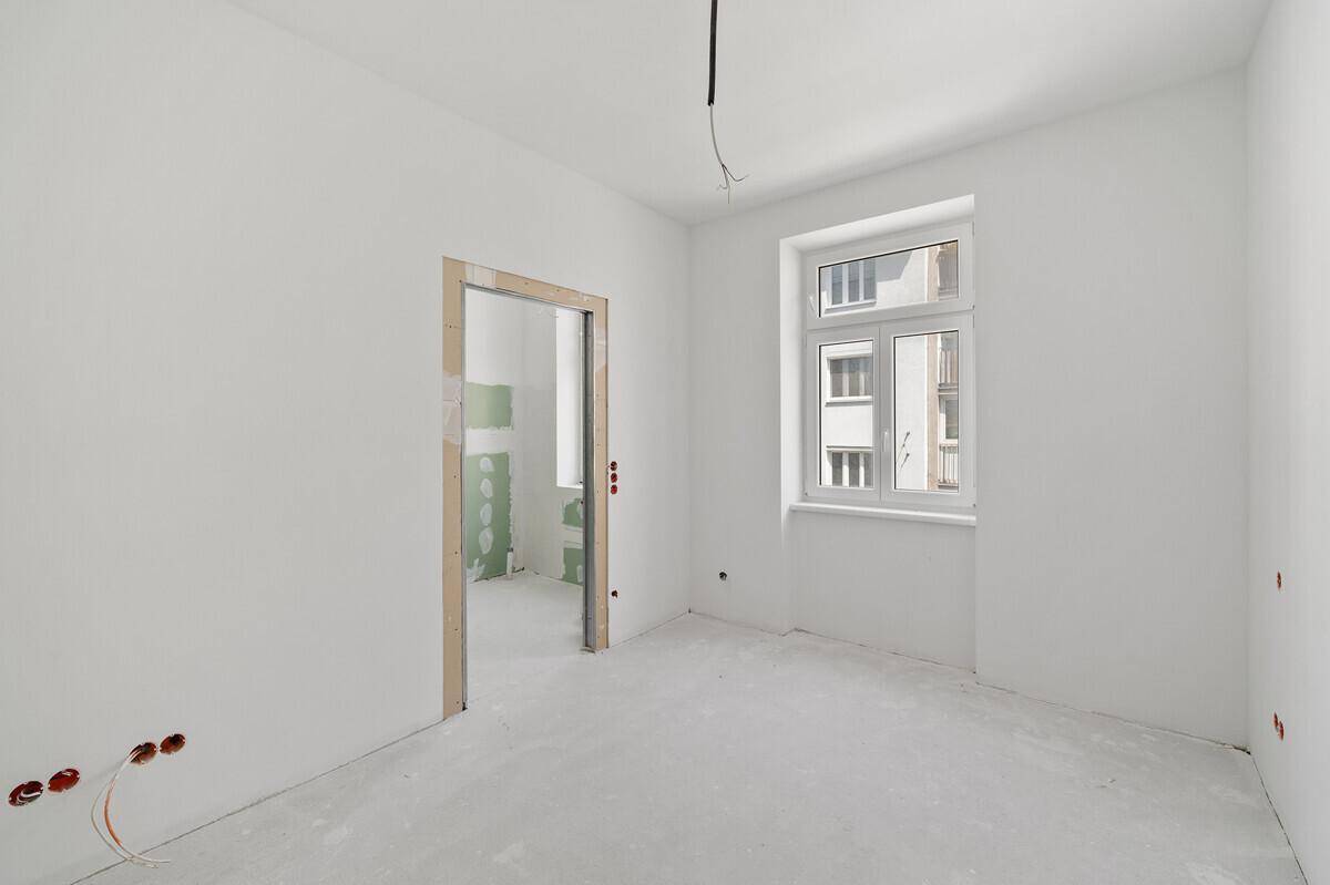 Helles Zimmer im Rohzustand mit Fenster und Blick auf den Innenhof, ideal für individuelle Gestaltung.