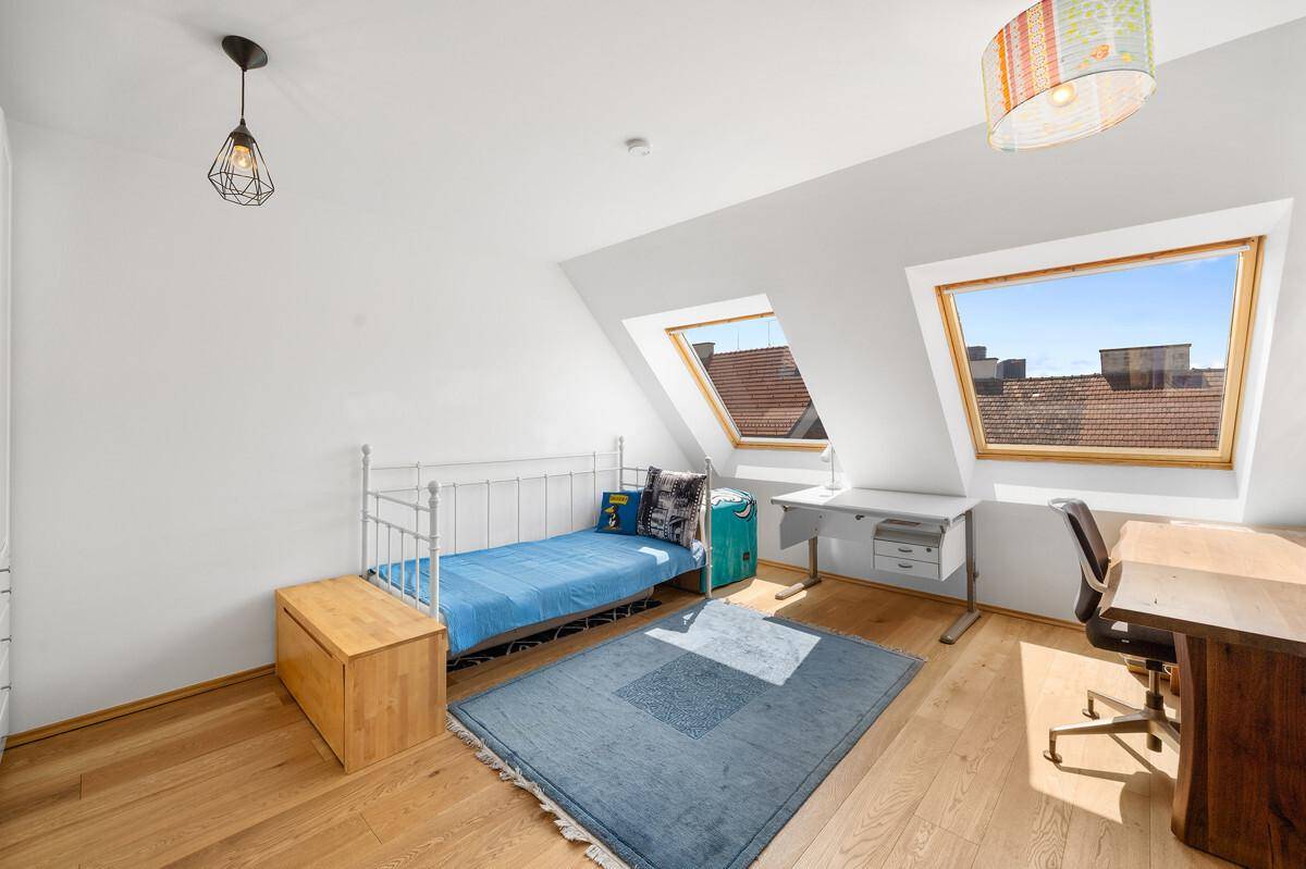 Schlafzimmer im Dachgeschoss mit Einzelbett, Schreibtisch und Holzboden.