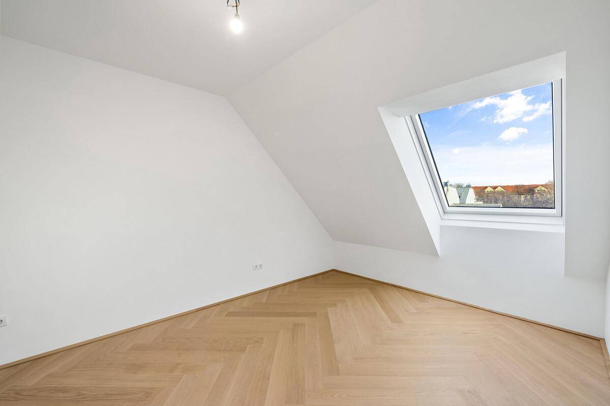 Lichtdurchfluteter Raum im Dachgeschoss mit schrägem Fenster und Parkettboden.
