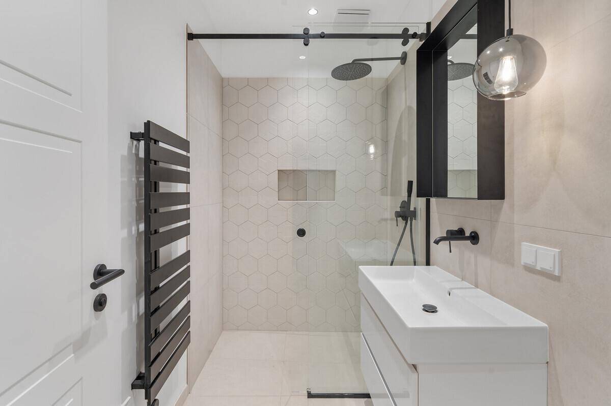 Helles Badezimmer mit begehbarer Dusche, modernen Fliesen und schwarzem Heizkörper.