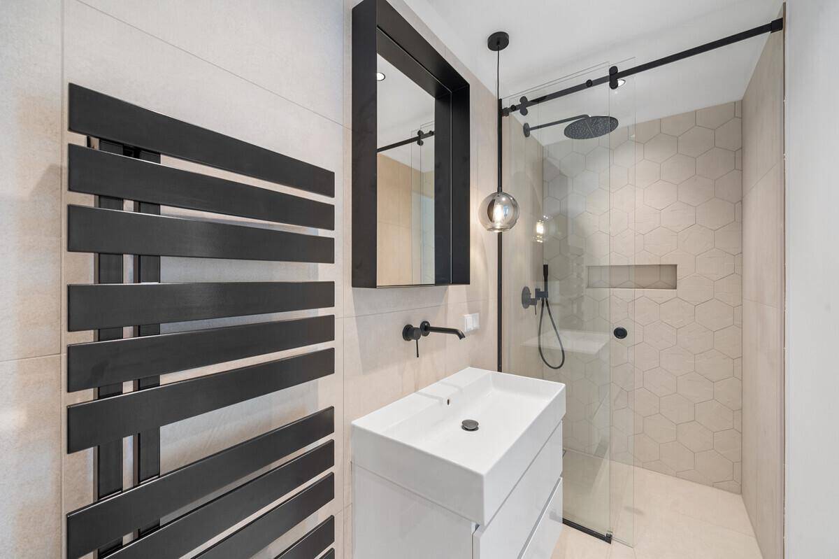 Modernes Badezimmer mit begehbarer Dusche, beheiztem Handtuchhalter und stilvollen schwarzen Armaturen.